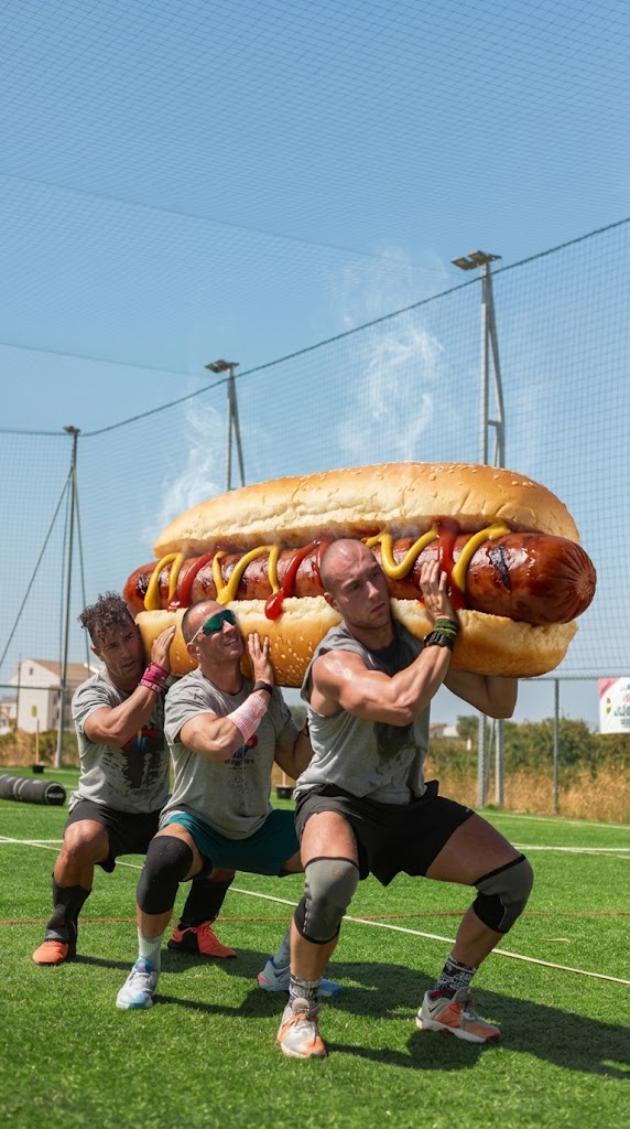 Tre atleti sollevano un hot dog gigante su un campo d'allenamento all'aperto